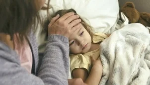 Child lying in bed with someone checking their temperature