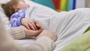 Child in bed holding someones hand