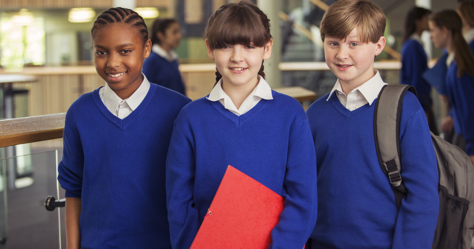 Image shows three school aged children in uniform, one is holding a red folder