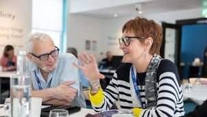  A man and woman are having a conversation at a table, both wearing Asthma + Lung UK lanyards