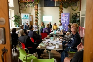 A group of people sit in a discussion circle at an indoor event, with banners for the Clean Air Justice Network and Asthma + Lung UK in the background