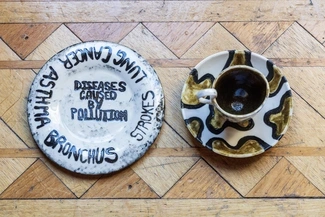 Two ceramic plates and a cup with an artistic design highlighting the impact of pollution, with one plate listing diseases like asthma, lung cancer, and strokes