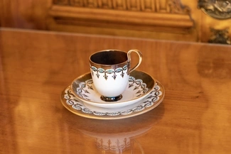 A decorative teacup with matching saucers, featuring intricate blue, brown, and gold patterns, placed on a polished wooden surface