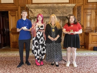 Four people stand in an ornate room, three holding teacups and saucers, with a mayor in the centre wearing a ceremonial chain